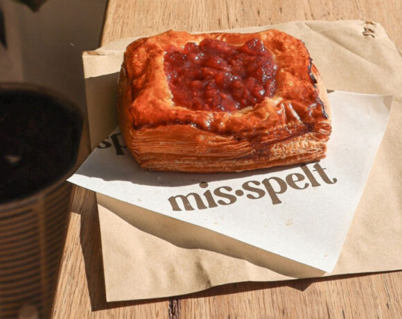 A square Danish filled with berry jam rests on a napkin with the words "Mis•spelt" on them, this in turn rests on a wooden countertop (Mis•spelt)