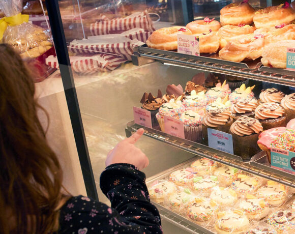 A young girl stands in front of a glass case full of baked sweets. She points to one of the items (Ferguson Plarre's Bakehouse)