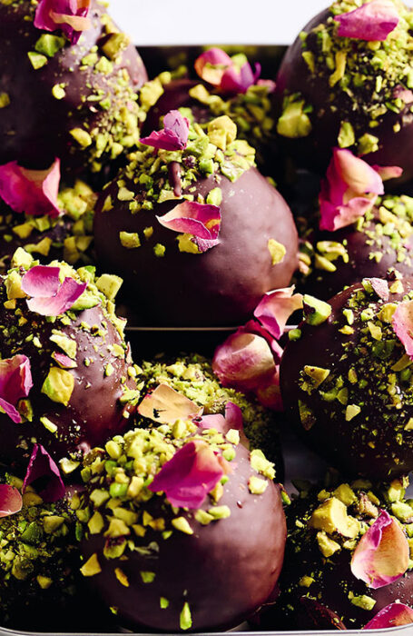 A metal lunch box full of delicious looking Turkish delight bites, covered in chocolate, pistachio crumbs and rose petals