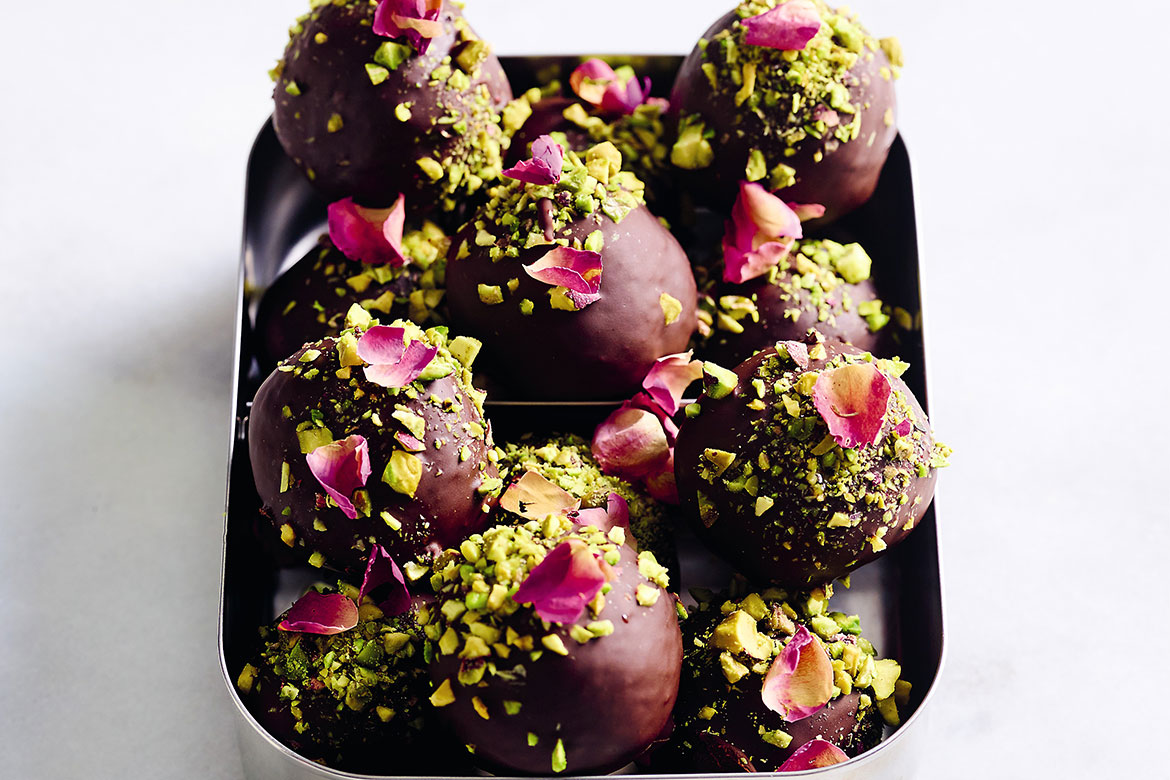A metal lunch box full of delicious looking Turkish delight bites, covered in chocolate, pistachio crumbs and rose petals