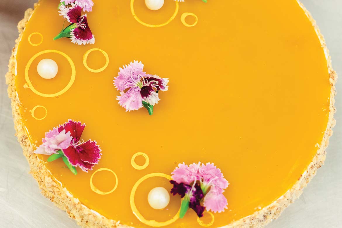 A top-down view of a beautiful mango cheesecake decorated with pearls and edible flowers