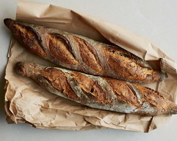 Two linseed baguettes lying on a paper bag