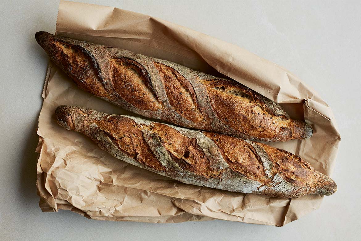 Two linseed baguettes lying on a paper bag