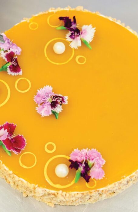 A top-down view of a beautiful mango cheesecake decorated with pearls and edible flowers