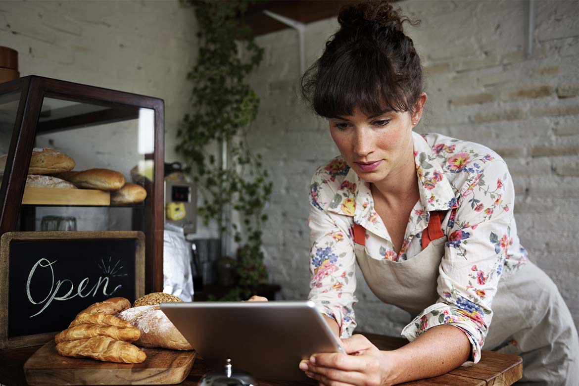 A woman leans against a shop counter holding a tablet (small business)