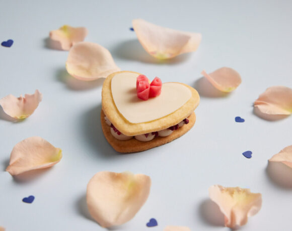 one heart-shaped sable mille feuille sitting on a white surface that is covered in light pink rose petals