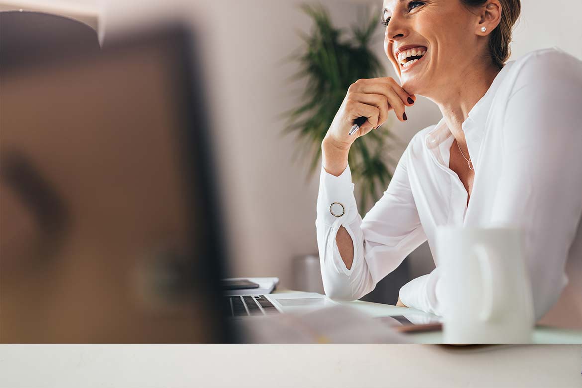 Smiling woman sitting at her desk in office. Happy business woman sitting in office with fingers touching her chin. (happiness)