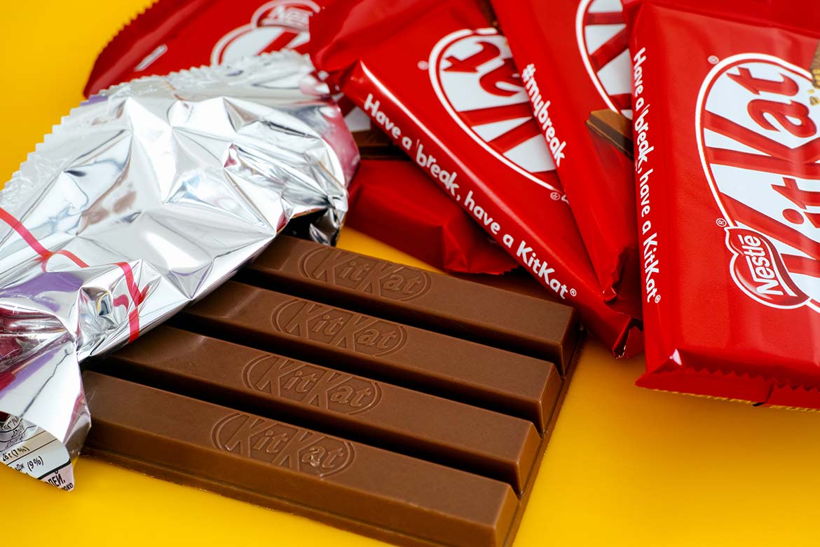 One open KitKat chocolate bar surrounded by other kitkat bars on a yellow background. (paperization)
