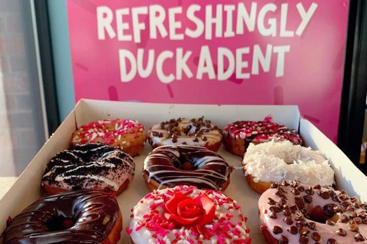 a box full of elaborately iced doughnuts with the sign 'refreshingly duckadent' above it (Duck Donuts)
