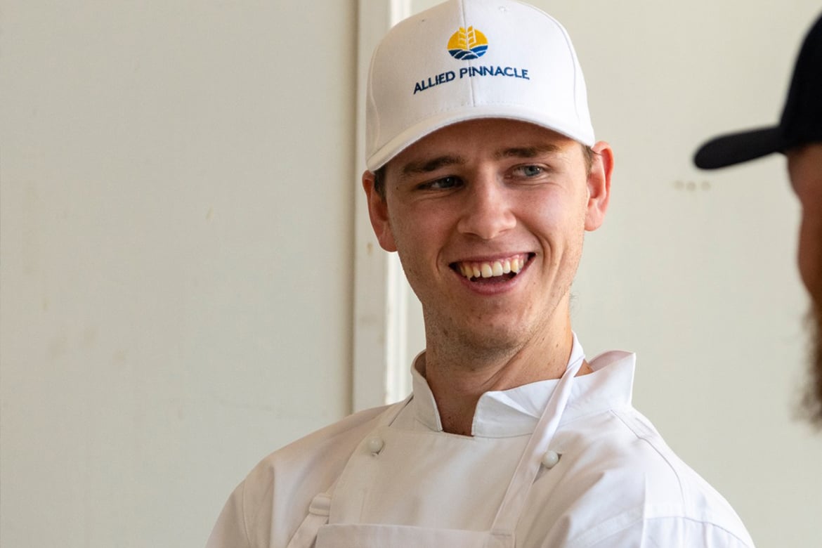 2023 LA Judge award winner Bjarke Svendsgaard smiles at a teacher talking to him. He wears chefs whites and a white cap.