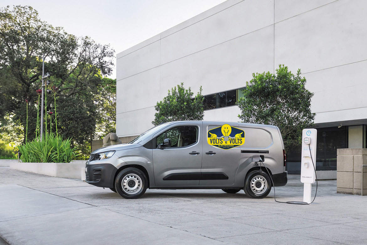 the Peugeot e-Partner Van is parked in front of a commercial building, plugged into an electric vehicle charger