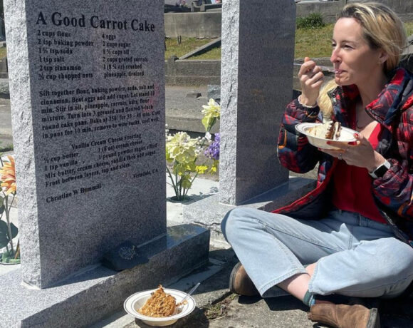 Rosie Grant sits in front of a grave eating a carrot cake, the recipe for which is inscribed on the headstone of the grave