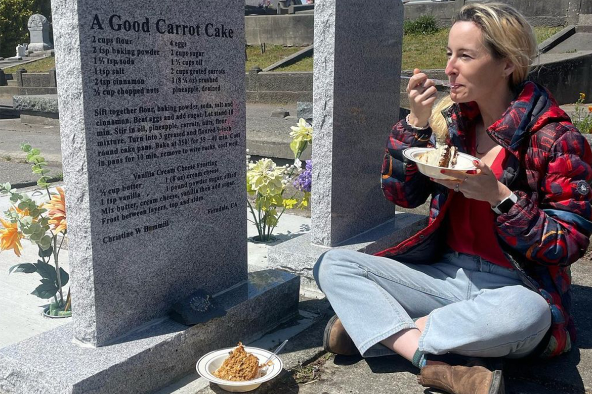 Rosie Grant sits in front of a grave eating a carrot cake, the recipe for which is inscribed on the headstone of the grave