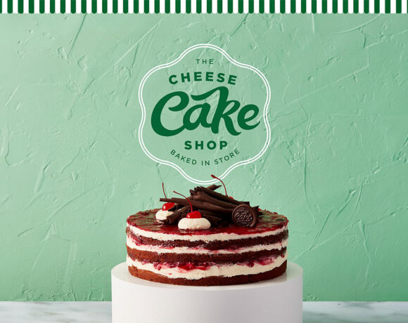 The Cheesecake Shop sign on a pale green background with a black forest cake in front