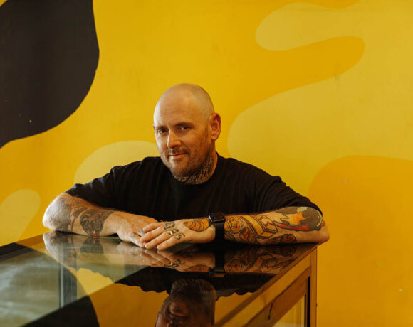 Jason Spencer from Banana Boogie leans on a glass counter in front of a yellow wall.