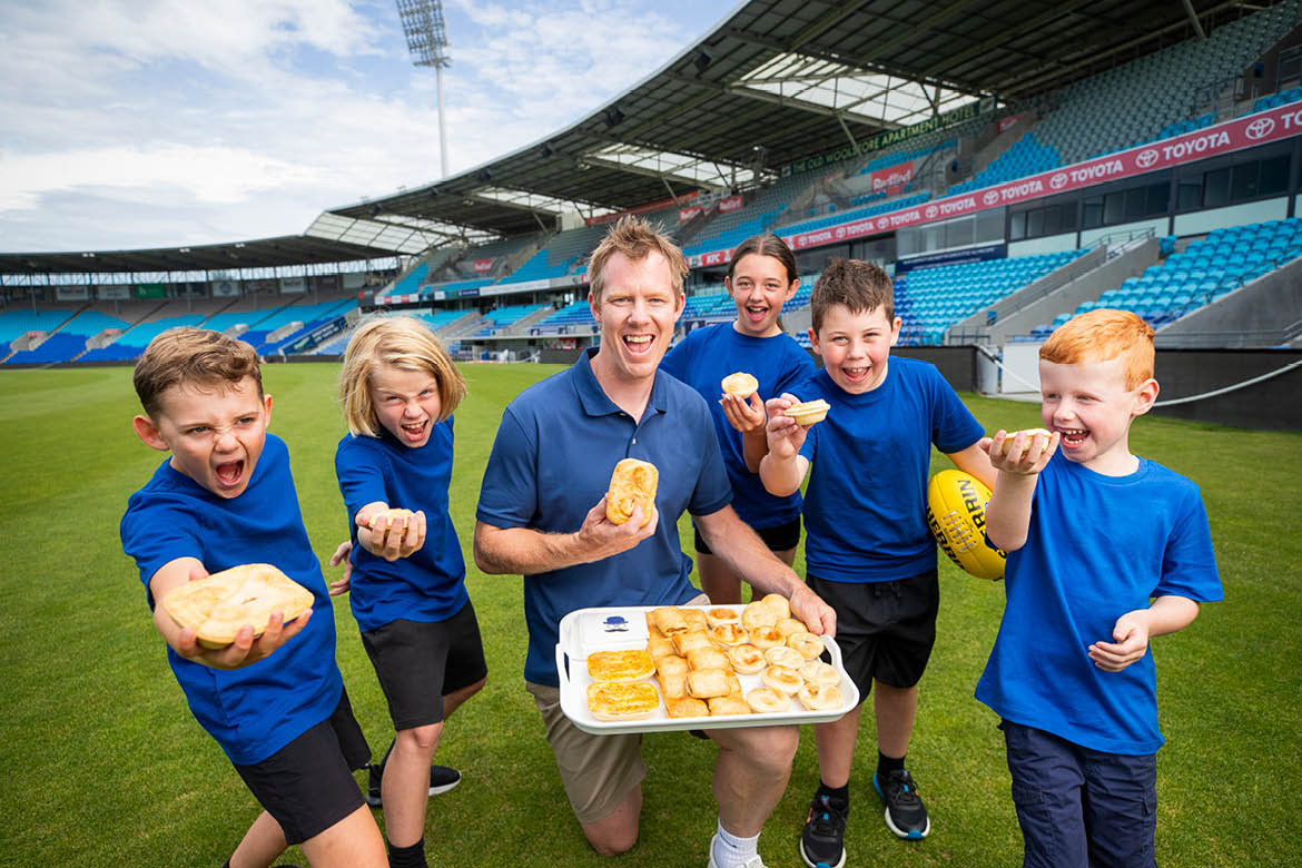 National Pies for Local Heroes is a campaign being run by Tasmanian Bakeries. Image features Campaign ambassador Jack Riewoldt holding a tray of pies, with five school children around him.