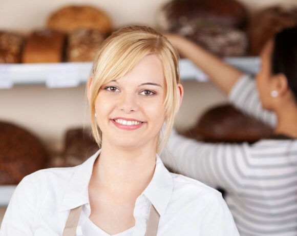 Victorian businesses are being urged to review rosters to remain in line with child employment laws. Image is of a blonde, white, female teeneager smiling at the camera while an older staff stock bread behind her.