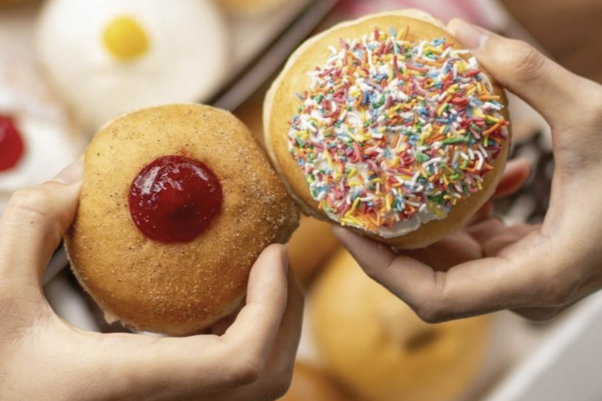 Two donuts are being held, one with jam and the other with rainbow sprinkles.