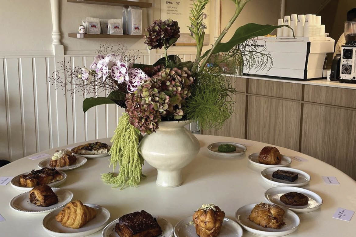 Pantry Story's unique table display. Pictured is a table with a white table cloth with white plate holding baked good. In the middle is a large floral display.