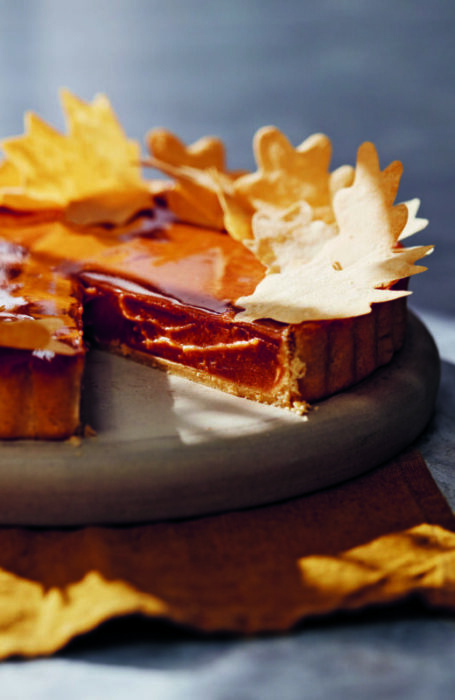 A sweet potato pie is sitting on a grey cutting board. A piece has been cut out. Decorative pastry leaves have been scattered on top.