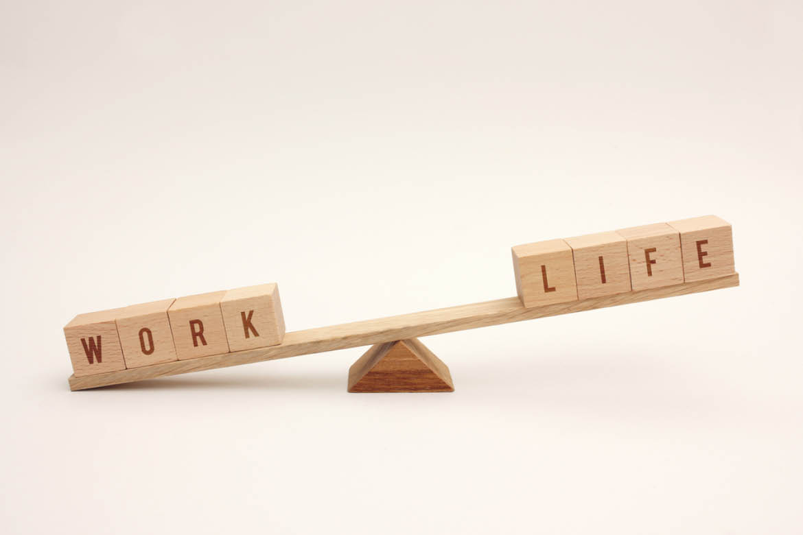 A wooden scale balances the words work and life. The work side is touching the counter.