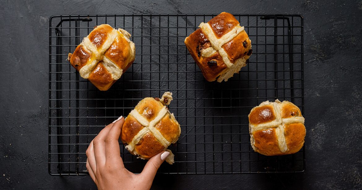 Persons hand reaching for a hot cross bun on a wire rack