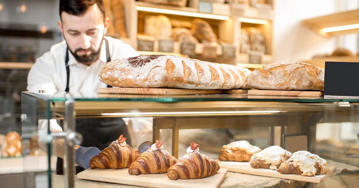 Man putting his baked goods into a display cabinet in a bakery