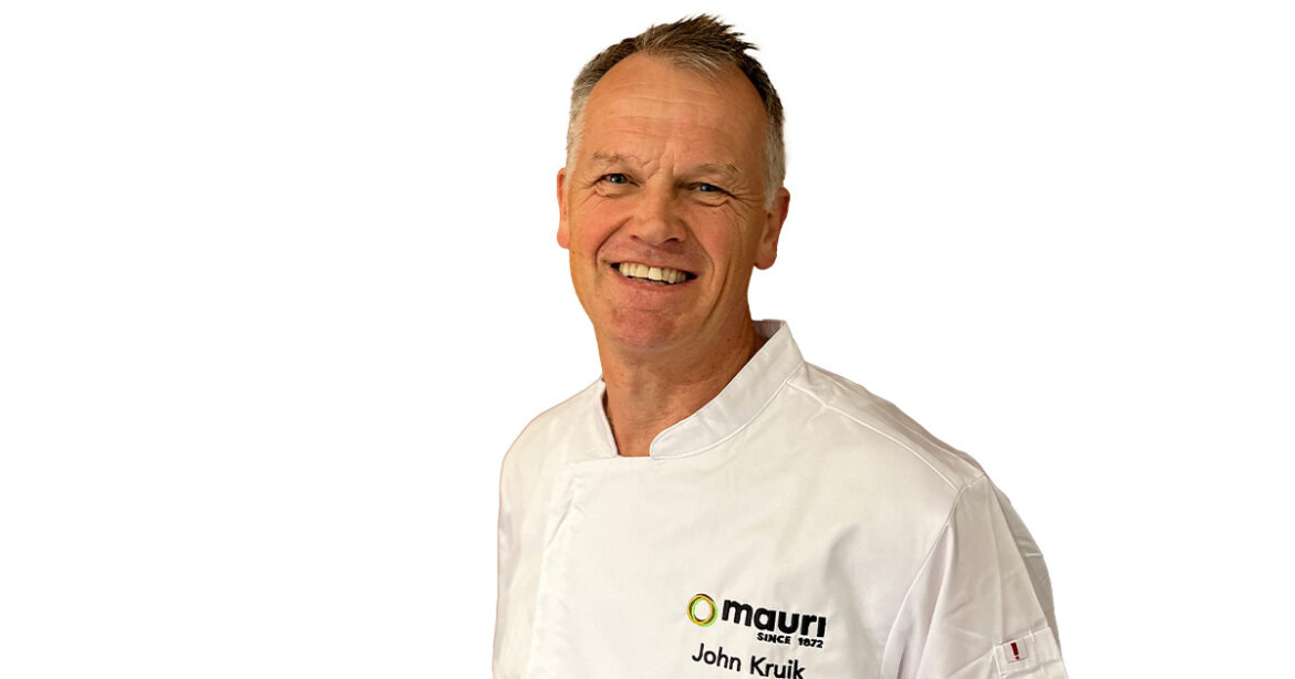 LA Judge John Kruik. Pictured is a middle ages man with greying hair. He's wearing chef whites and is smiling at the camera.