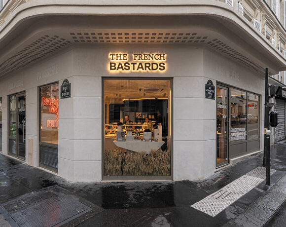 The French Bastards are taking on tradition. Pictured is the shopfront of a The French Bastards store. It's grey, with wet pavement out the front. Inside it lit up and you can see two employees serving customers.