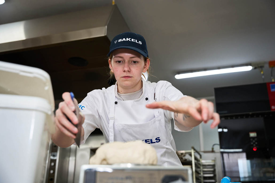 LA Judge winner Imogen Fearon is reaching towards the camera across the kitchen bench. She's reaching for dough and has a look of concentration on her face.