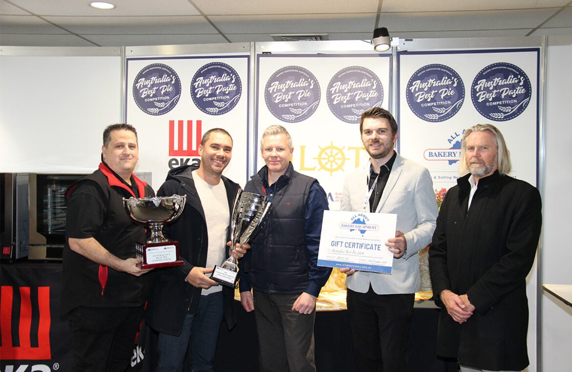 Rolling Pin Pies owner Nathan Williams has taken out the 2024 Best Pie award at the Baking Industry Trade Show. Pictured are 5 men, all in suits. They are smiling at the camera. Nathan, second from the left, is holding a large silver trophy.