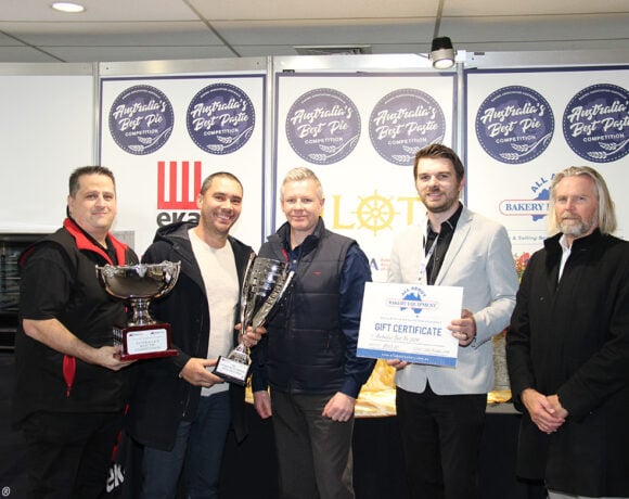 Rolling Pin Pies owner Nathan Williams has taken out the 2024 Best Pie award at the Baking Industry Trade Show. Pictured are 5 men, all in suits. They are smiling at the camera. Nathan, second from the left, is holding a large silver trophy.