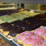 Pictured is a cabinet full of donuts at Donut Papi. Some have pink icing and rainbow sprinkles, while others have chocolate icing.