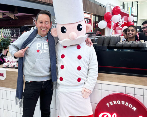 Ferguson PLarre CEO Steve Plarre wears a grey jumper with the word pie across teh front. He stands with a person dressed up as the Ferguson Plarre mascot.