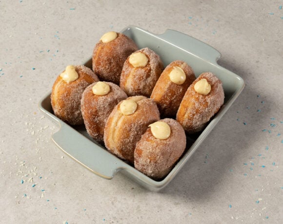 Doughnuts made using MOI International's Doughmax. Pictured are eight doughnuts in a blue baking dish. They are all up on end, with cream coming out of the top.