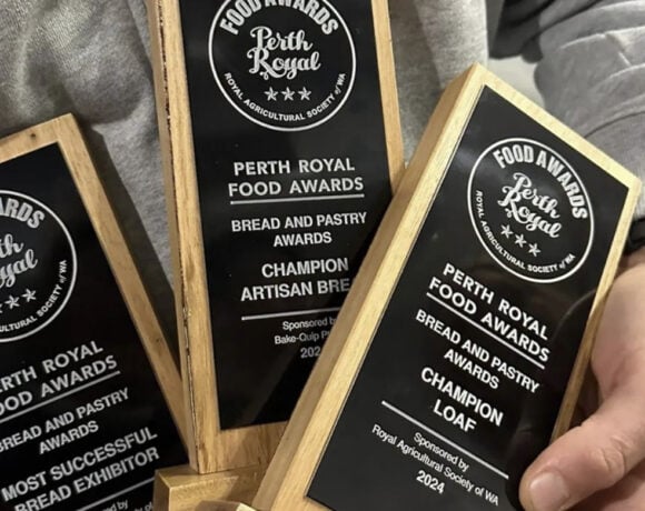 Three gold trophies with black plaques are held in two hands. The trophies all say Perth Royal Food Awards across the top.