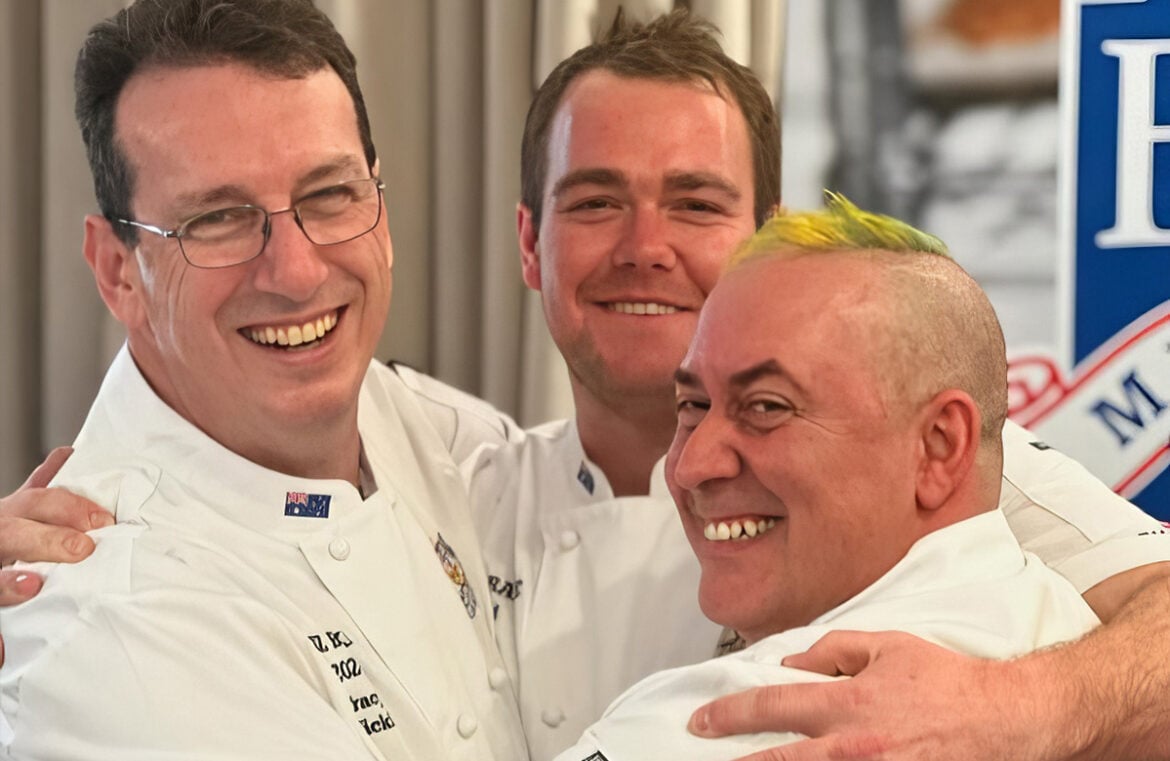 Brad Burkitt (centre) with his ANZBake team mates Tracy Nickl (left) and Jeremy Mavromatakis (right). They're all hugging and smiling at the camera