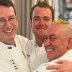 Brad Burkitt (centre) with his ANZBake team mates Tracy Nickl (left) and Jeremy Mavromatakis (right). They're all hugging and smiling at the camera