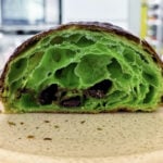 A bright green croissant has been cut in half. It sits on a white plate held by a hand.