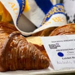 Adelaide's Finest Supermarkets' winning croissant sits on white tray. Behind it is a blue and white ribbon.