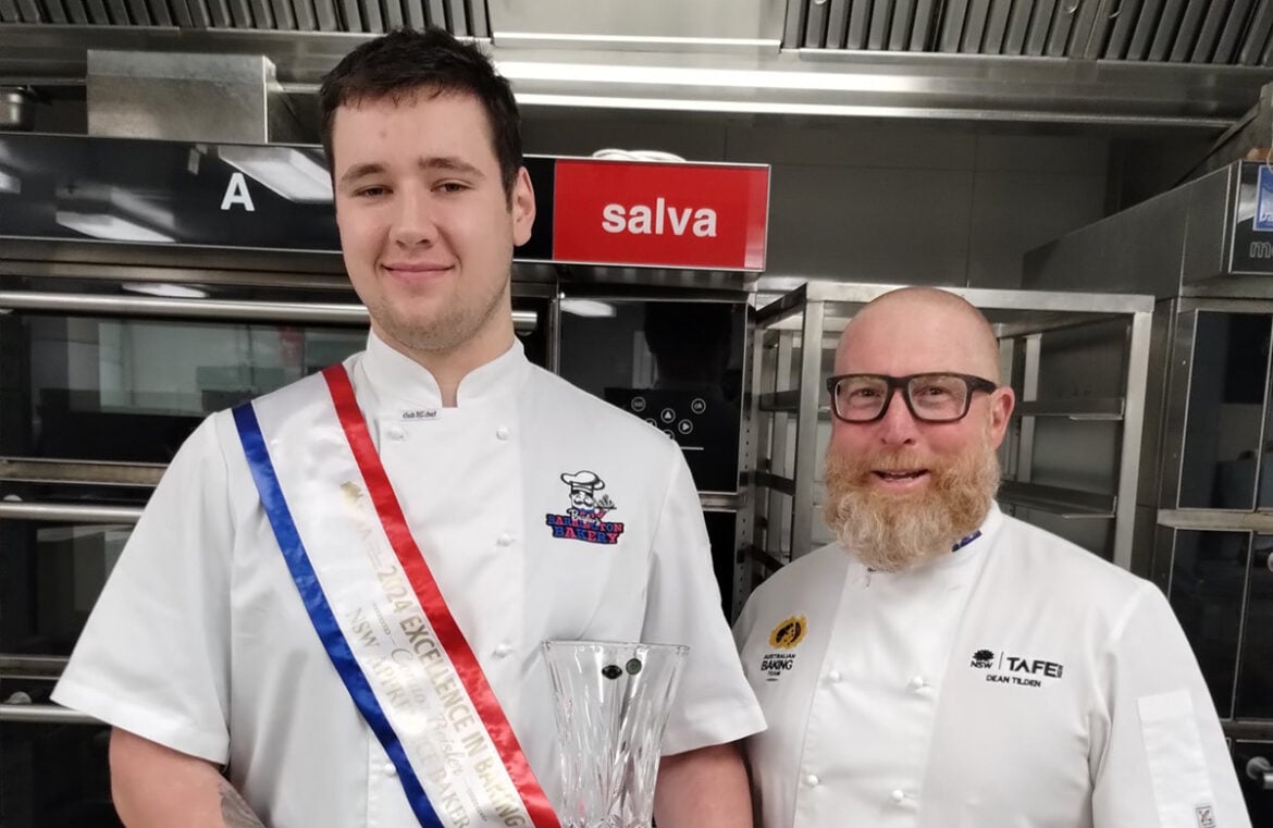 Connor Beisler stands with his teacher, Dean Tilden. Tbey both wear baking whites. Connor wears the red, white, and blue sash for Excellence in Baking