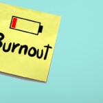 How can a business owner avoid burning out? pictured it a blue background with a yellow post it note on it. There's a picture of a battery on low with the word burnout written underneath
