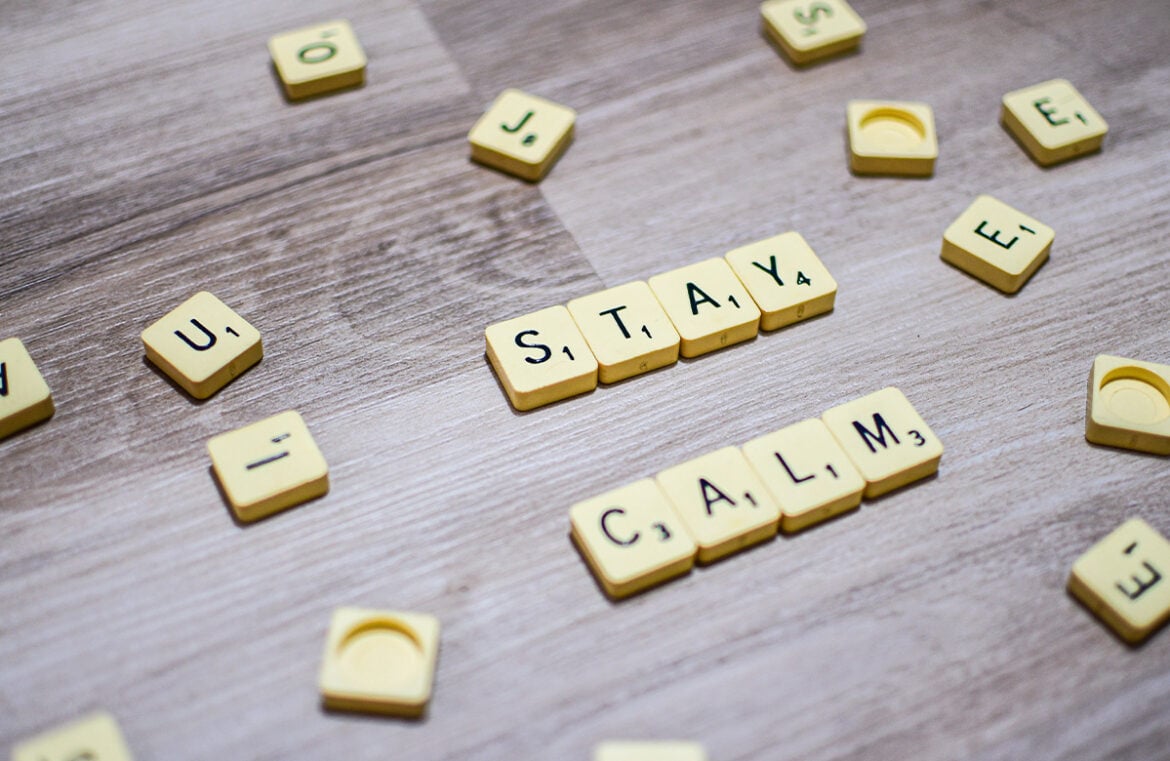 Having practices in place can help you weather the tough times better. Pictured is a wooden table with scrabble pieces strewn across the top. The words Stay Calm are spelled out