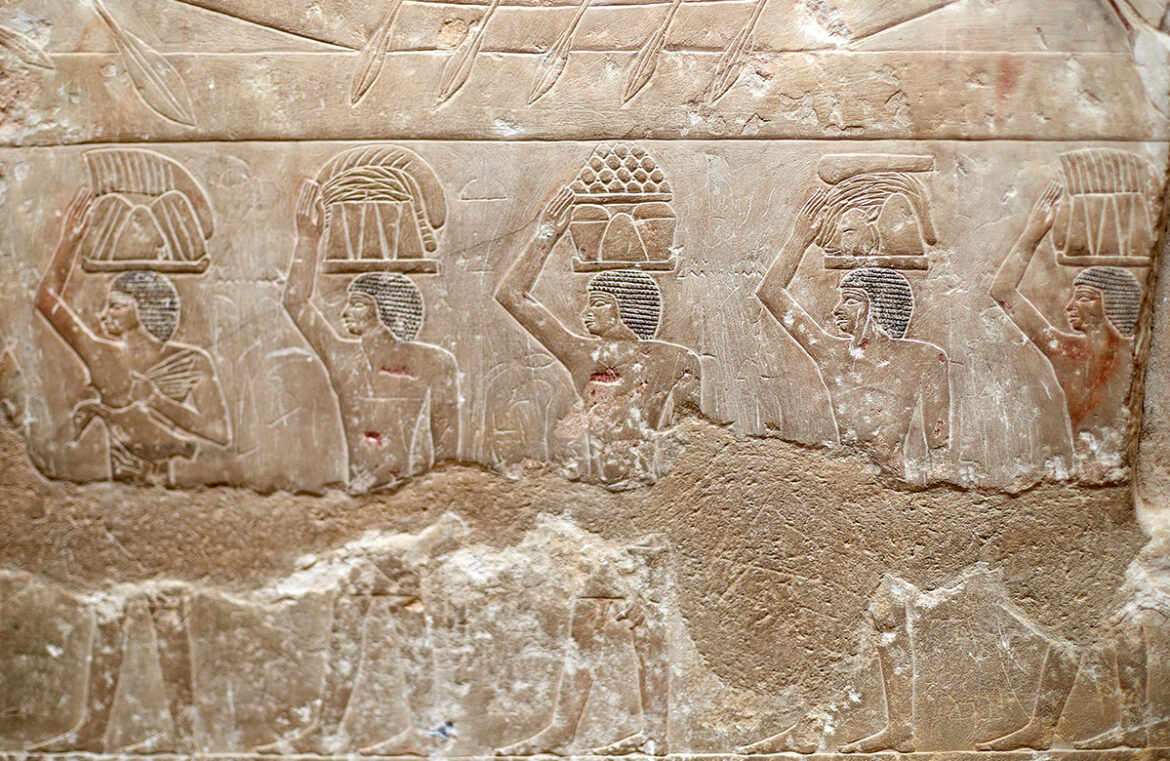 A procession of men carrying food offerings on their heads.