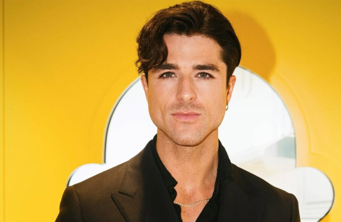 Donut Daddy aka Anthony Randello-Jahn will be attending the Baking Industry Trade Show in June. Pictured is Anthony, a white man with short dark hair and dark eyes. He's wearing a black suit and standing in front of a bright yellow background. He's not smiling.