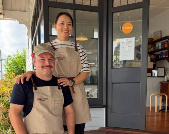Paul and Miki from newly opened Atelier Mimi. Pictured is a man and woman standing on wooden stairs. The man is white with dark hair. He's earing a tan apron and cap. The woman has dark hair and is wearing a striped shirt and tan apron. They are both smiling at the camera.