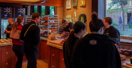 Shadow Baking's newest location in North Adelaide has opened its doors. Pictured is a warm bakery with wooden counters and warm lighting. It is full of people looking at glass counters full of baked goods