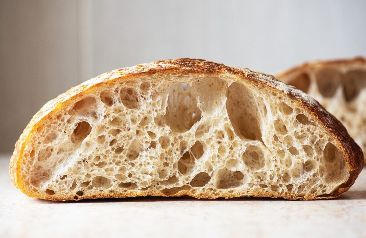 Scientists have successfully baked a sourdough loaf using yeast harvested from a 5000-year-old mummy. Pictured is a loaf of sourdough cut in half. It's sitting on a white counter with a white tiled background.