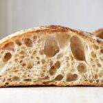 Scientists have successfully baked a sourdough loaf using yeast harvested from a 5000-year-old mummy. Pictured is a loaf of sourdough cut in half. It's sitting on a white counter with a white tiled background.