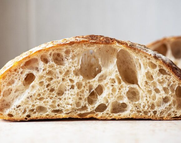 Scientists have successfully baked a sourdough loaf using yeast harvested from a 5000-year-old mummy. Pictured is a loaf of sourdough cut in half. It's sitting on a white counter with a white tiled background.